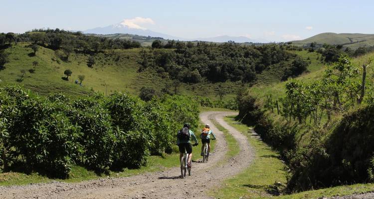 Deux cyclistes sur un sentier de terre à travers un paysage verdoyant avec vue sur la montagne.