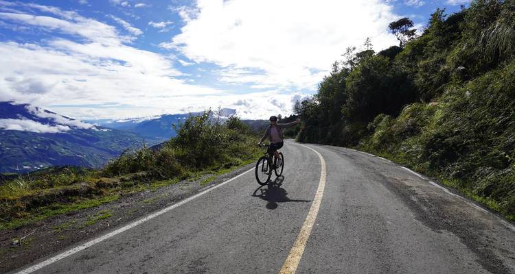 Un cycliste sur une route pavée avec vue sur les montagnes et un ciel nuageux.