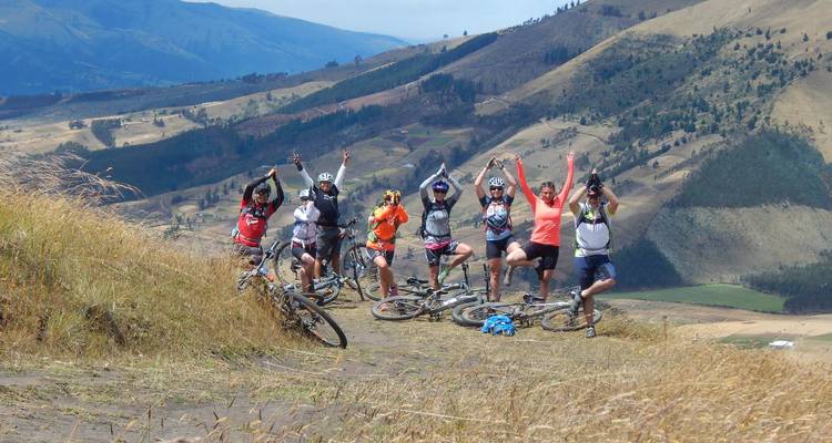 Groupe de cyclistes posant sur une colline avec vue sur des collines ondulantes.