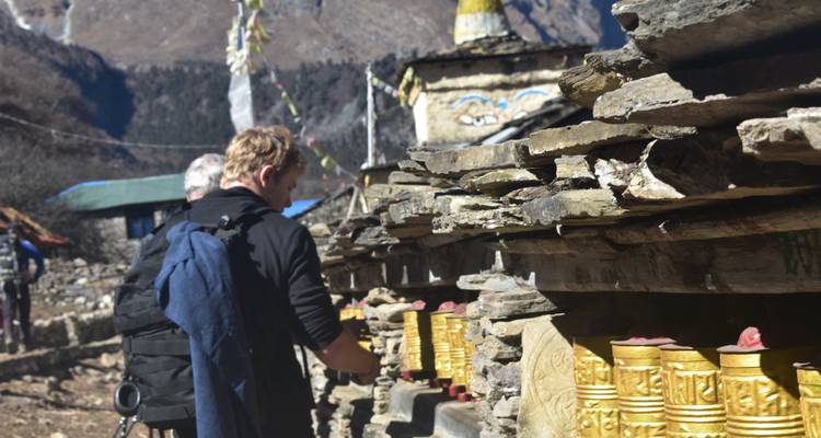 Los trekkers giran ruedas de oración doradas colocadas en un muro Mani de piedra en un remoto pueblo de montaña nepalí.