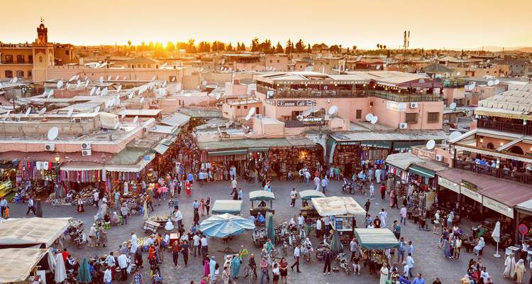 Bustling market square in Marrakesh at sunset with people and vibrant stalls.
