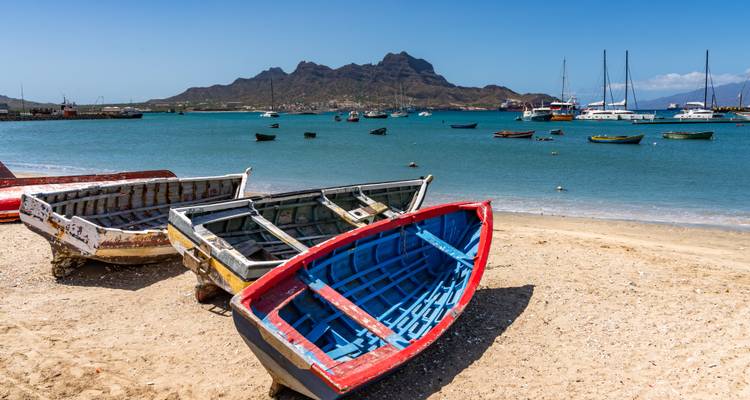 Des bateaux de pêche colorés sur une plage de sable avec un arrière-plan montagneux.