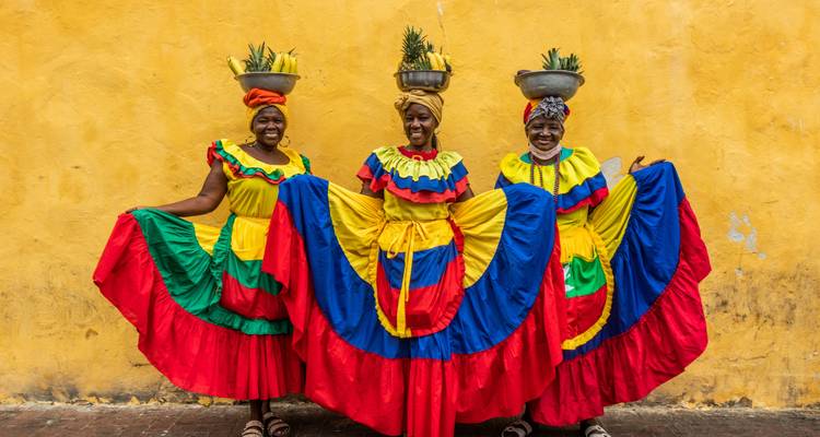 Femmes en robes traditionnelles colorées posant avec des paniers de fruits sur la tête.