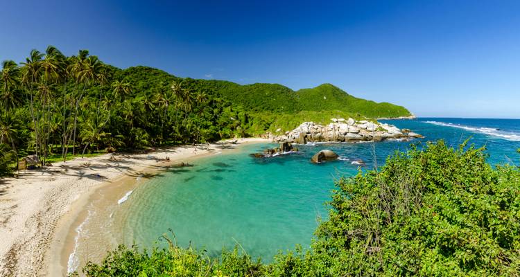 Plage immaculée avec une eau turquoise et des collines verdoyantes luxuriantes.