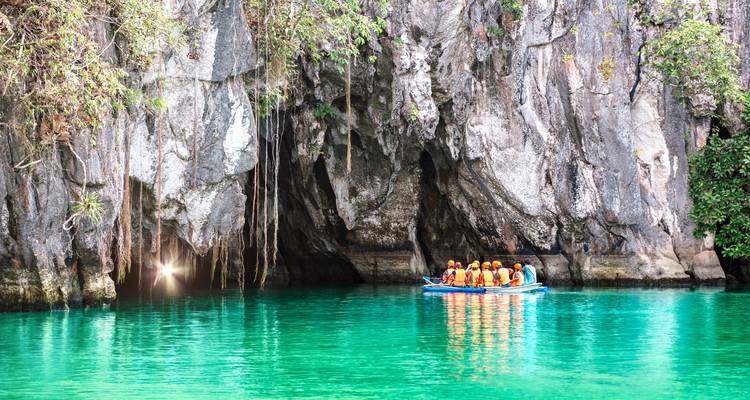 Des touristes dans un bateau visitant une rivière souterraine aux eaux turquoise claires.