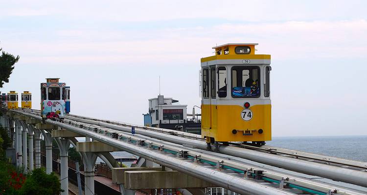 Yellow tram on an elevated track by the sea.