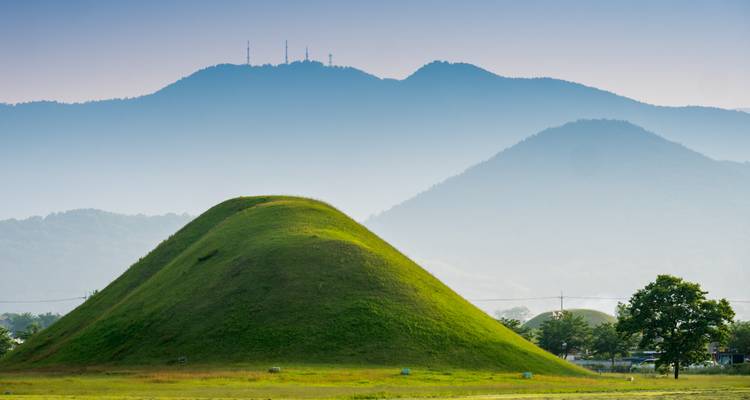 Green mound with a mountainous backdrop under a clear sky.
