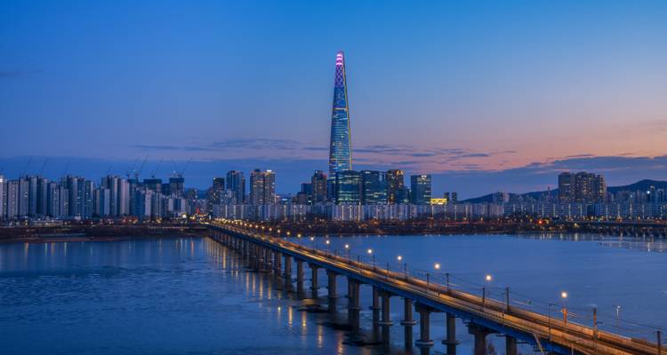 City skyline at night with a lit bridge and river.