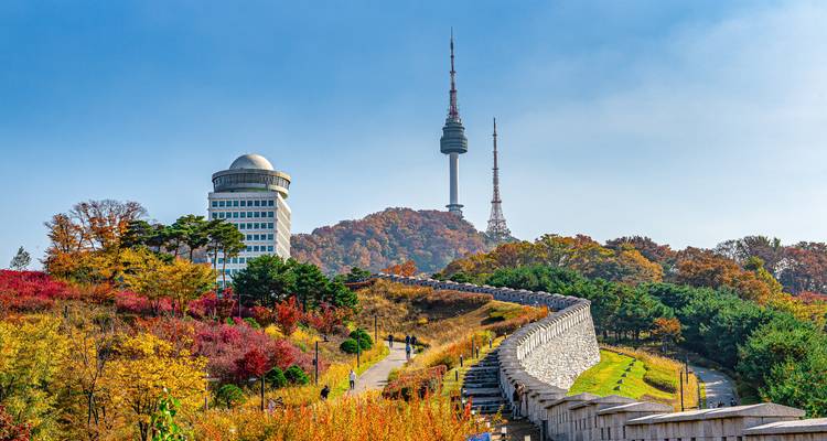 Namsan Seoul Tower against a forested hillside during autumn.