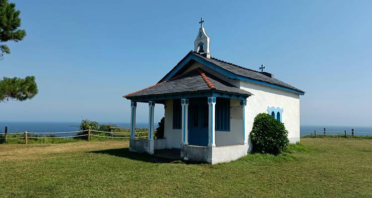A small picturesque chapel on a grassy hill overlooking the sea.