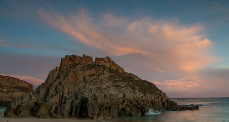 A dramatic rocky coastline at sunset with vibrant skies.
