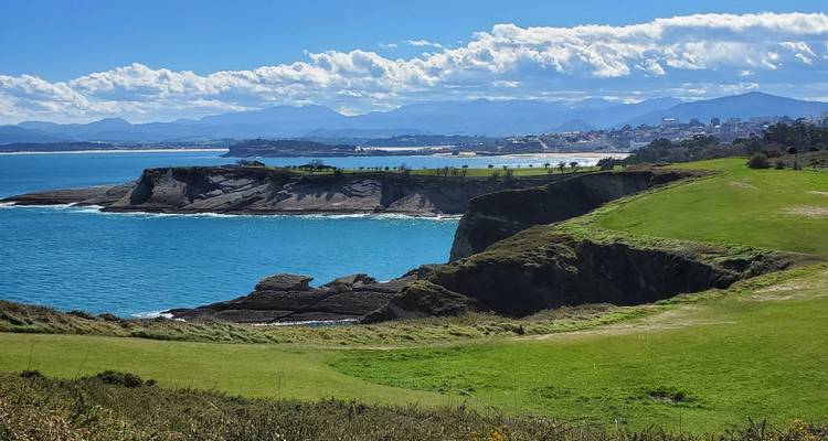 Falaises côtières avec mer bleue et montagnes lointaines.