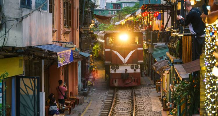 Train passant dans une rue étroite avec des gens qui prennent des photos.