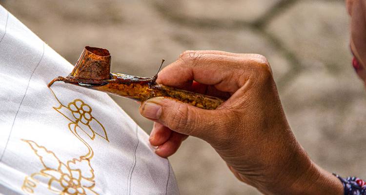 Person holding a canting tool for batik textile art.