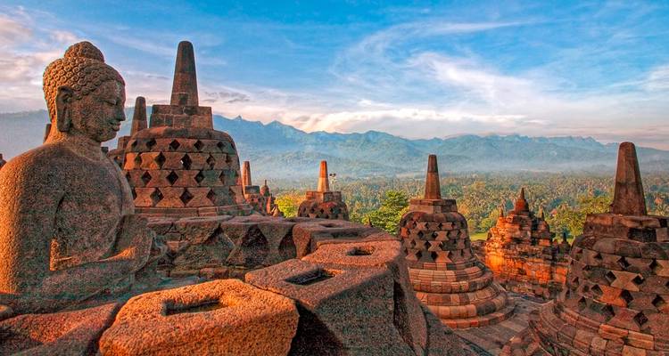 Borobudur Temple with stupa structures at sunrise and misty forest backdrop.
