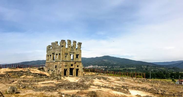 Antike Steinstruktur auf einem Hügel mit Bergkulisse.