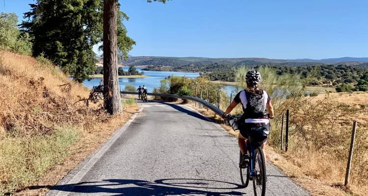 Radfahrer auf einer Straße in der Nähe eines Sees mit sanften Hügeln im Hintergrund.