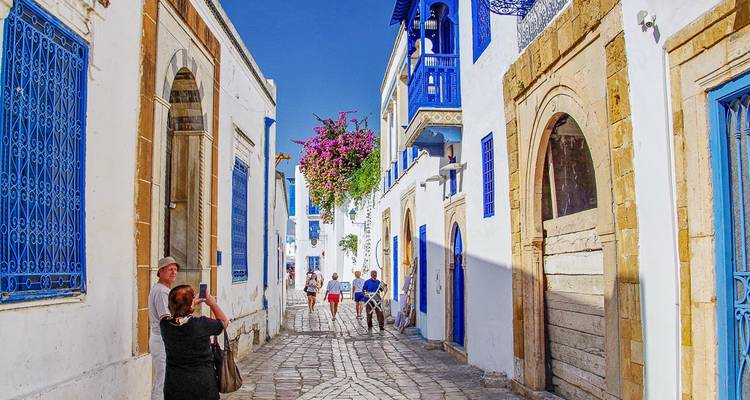 Des gens marchant dans une rue avec des bâtiments blancs et bleus.