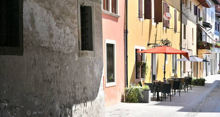 Kleurrijke gebouwen langs een rustige straat met buitenterrassen en parasols.