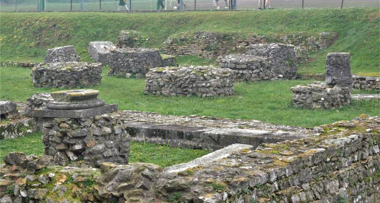 Oude stenen ruïnes op groen gras met een hek op de achtergrond.