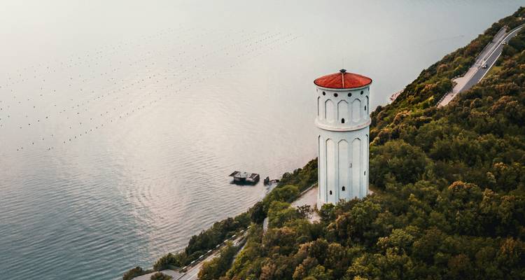 Witte toren met een rood dak die uitkijkt over een groot wateroppervlak.
