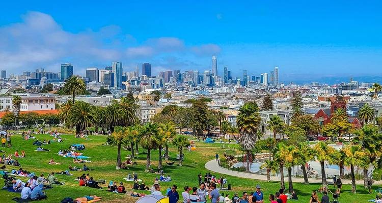 A city park with people enjoying a sunny day and a skyline view.