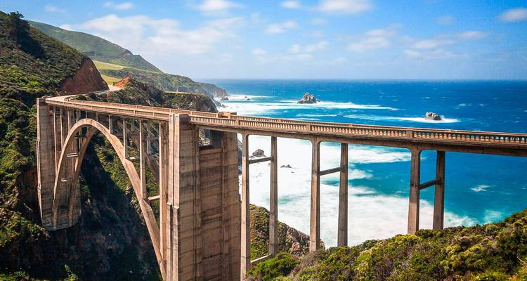 A large arch bridge spanning over a picturesque coast with wavy sea and scenic cliffs.
