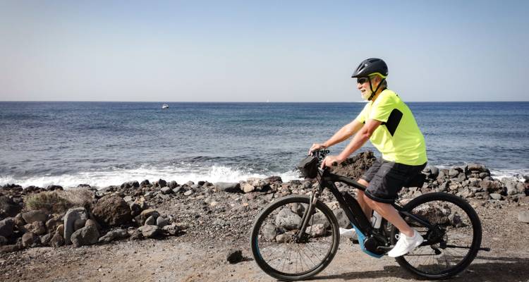 Person biking along a rocky coastline with waves crashing on the shore.