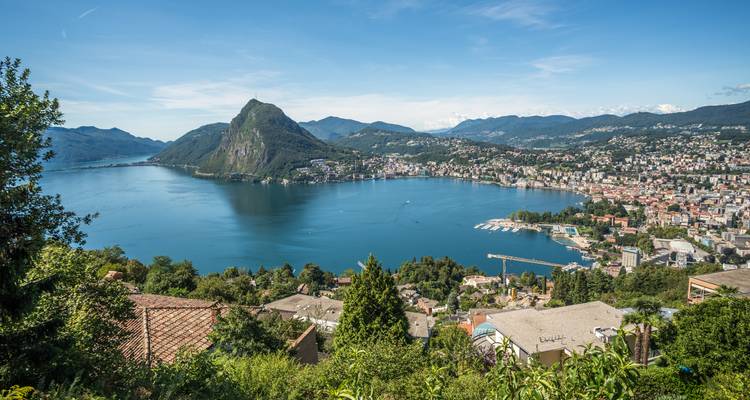 Panoramablick auf einen tiefblauen See, umgeben von Bergen und einer weitläufigen Stadt