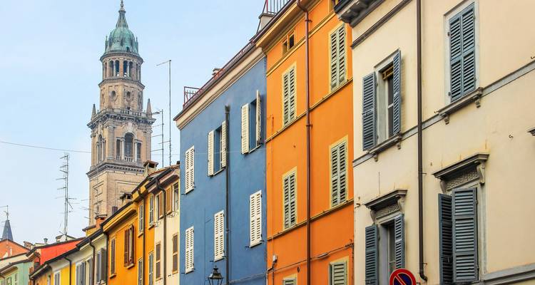Reihe pastellfarbener Stadthausfassaden mit Fensterläden neben einem historischen Glockenturm
