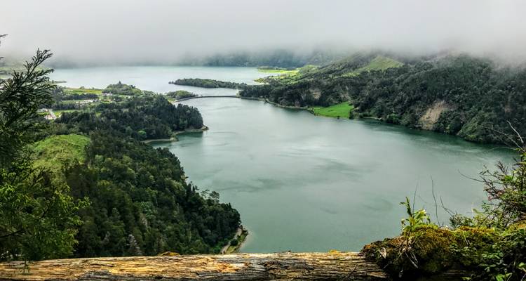 Vue aérienne d'un lac brumeux entouré de collines boisées.