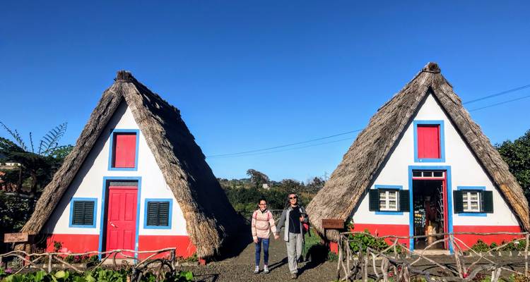Two people standing in front of traditional triangular thatched-roof houses.