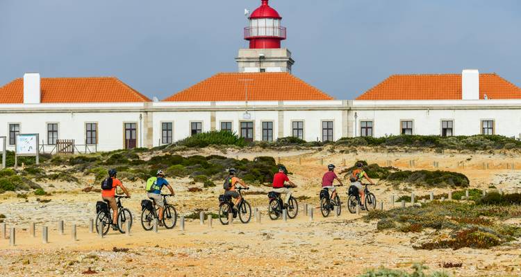 Cyclists approaching a lighthouse with a red roof.
