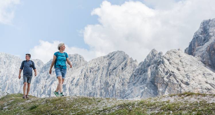 Twee wandelaars die langs een bergkam lopen met ruige bergen op de achtergrond.