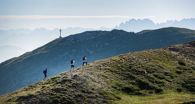 Wandelaars op een grasrijke heuveltop met een panoramisch uitzicht op verre bergtoppen.