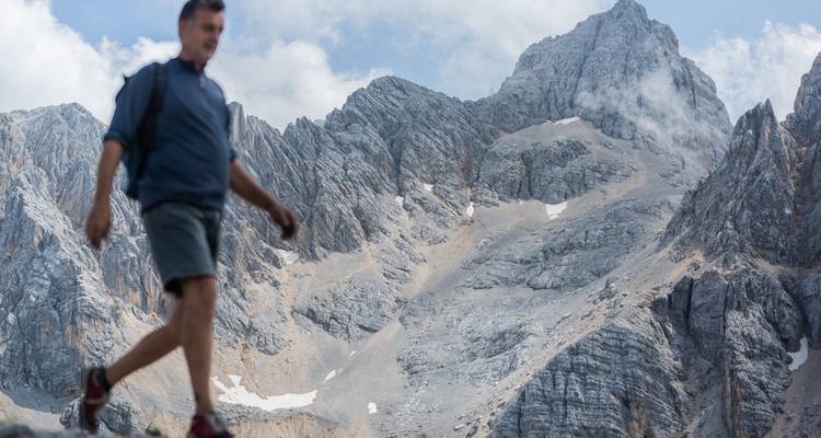 Wandelaar lopend voor ruig berglandschap.