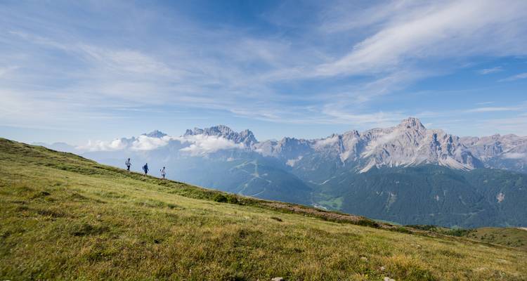 Drie wandelaars die een bergkam oversteken met een adembenemend uitzicht op valleien en bergtoppen.
