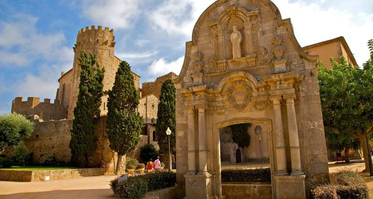 Een historisch bouwwerk op een klein plein met bomen en een heldere hemel.