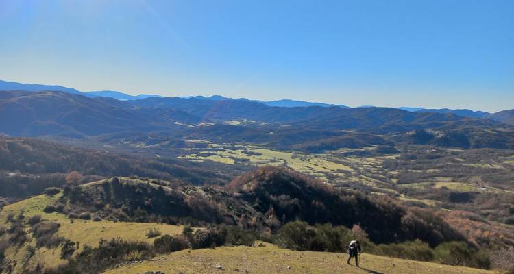 Een persoon die op een heuveltop staat en uitkijkt over een uitgestrekte vallei met bergen in de verte.