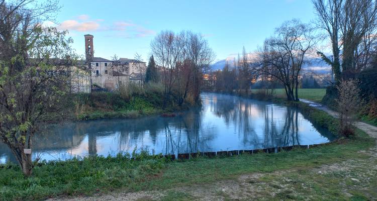 Een rustige rivier die door een landschap stroomt met kale bomen en een stenen gebouw.