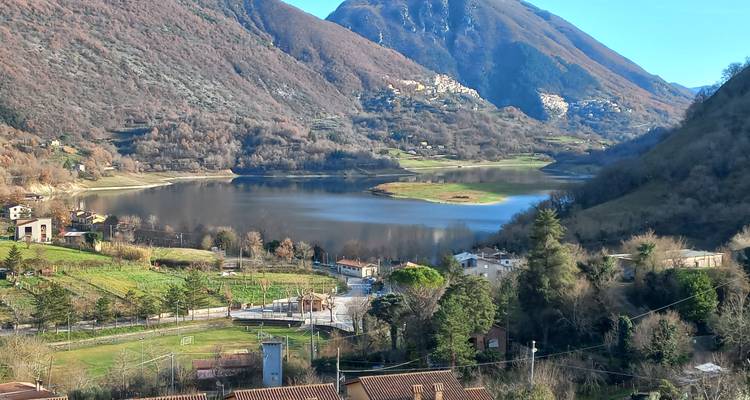 Een meer omringd door heuvels en kleine gebouwen onder een heldere hemel.