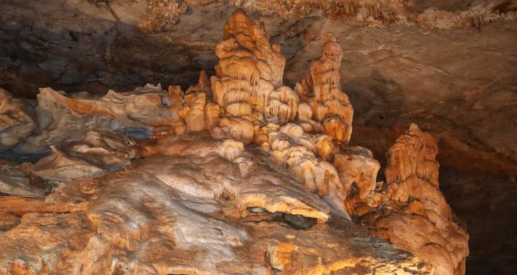 Gros plan de formations spectaculaires de stalactites et de dépôts calcaires éclairés par une lumière artificielle chaleureuse.