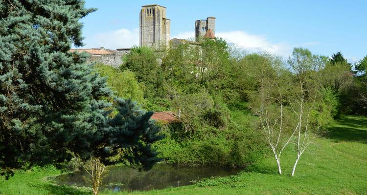 Deux hautes tours de pierre visibles au-dessus des arbres, avec un étang au premier plan.