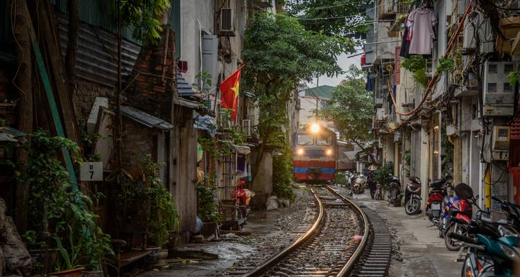 Train passing through narrow street lined with buildings in Vietnam.