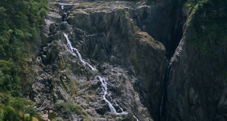 Waterfall cascading down a rocky cliff with greenery surrounding.