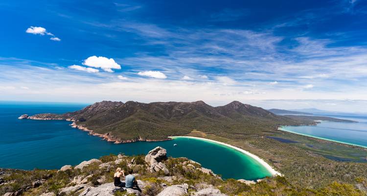 Aerial view of Wineglass Bay in Tasmania, Australia with hikers sitting on rocks in the foreground.