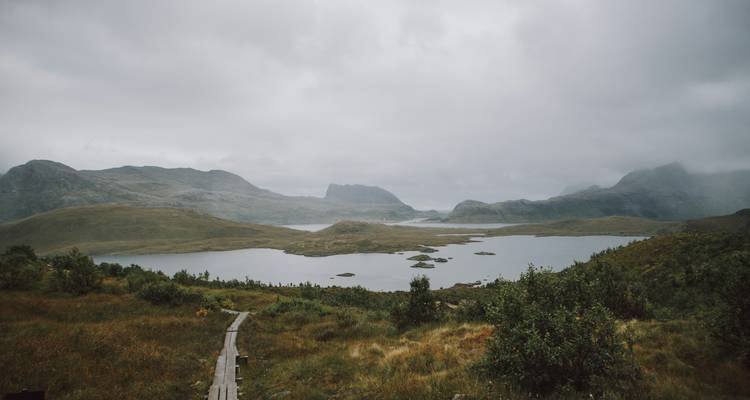 Misty mountains under a cloudy sky with a lake.