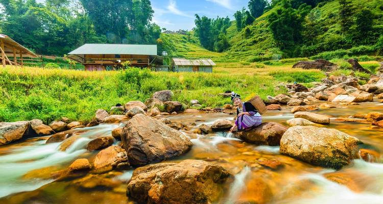 Two people by a rocky stream with lush green surroundings.