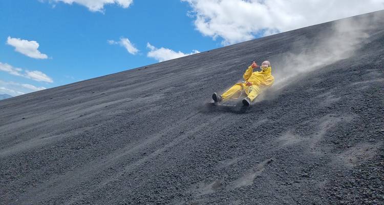 Person sliding down a black sandhill in a yellow suit.