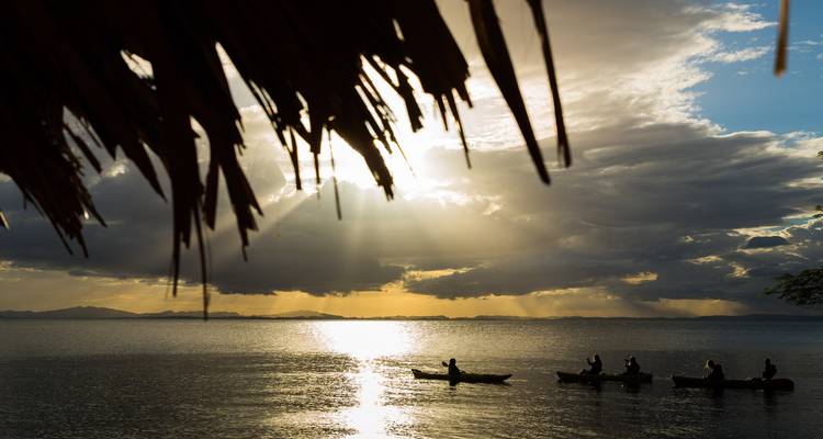 Silhouette of people in boats on a calm lake during sunset.